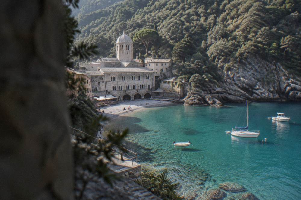 Clear turquoise water over pale pebbles in a small bay with pine covered cliffs on both sides