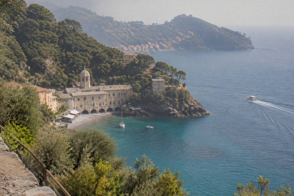 A small boat crossing open blue water toward a wooded headland with a village just visible in the bay beyond