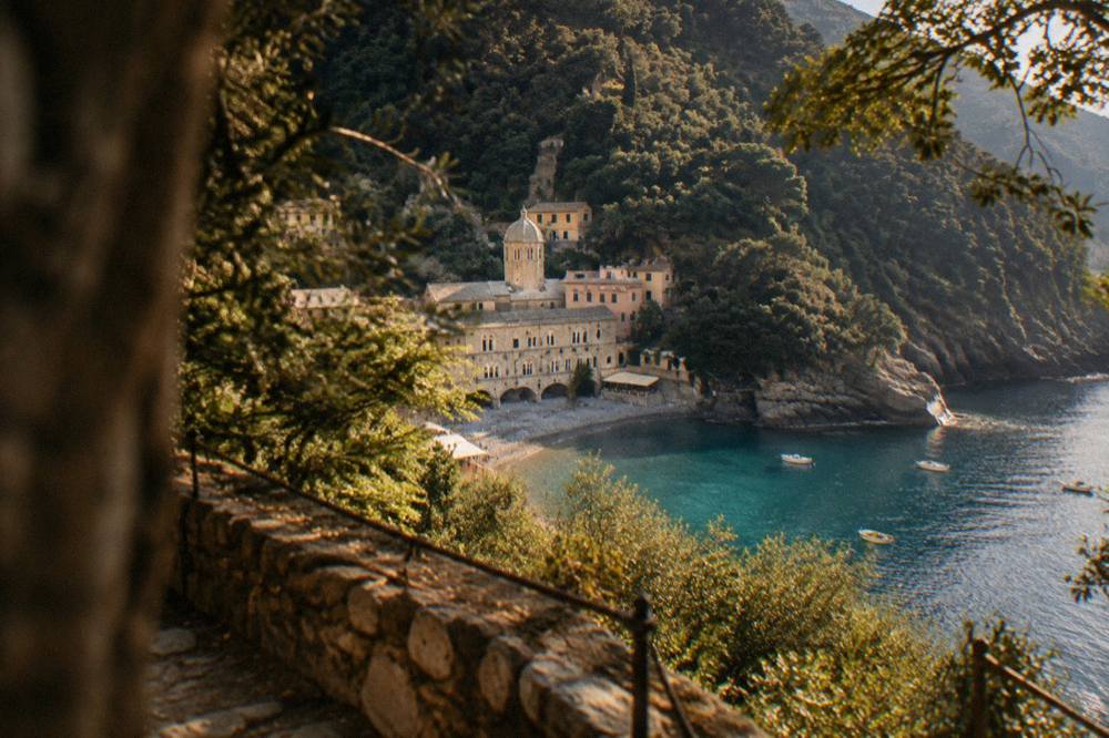 View from a wooded cliff path down onto a tiny bay with an abbey and a scattering of rooftops