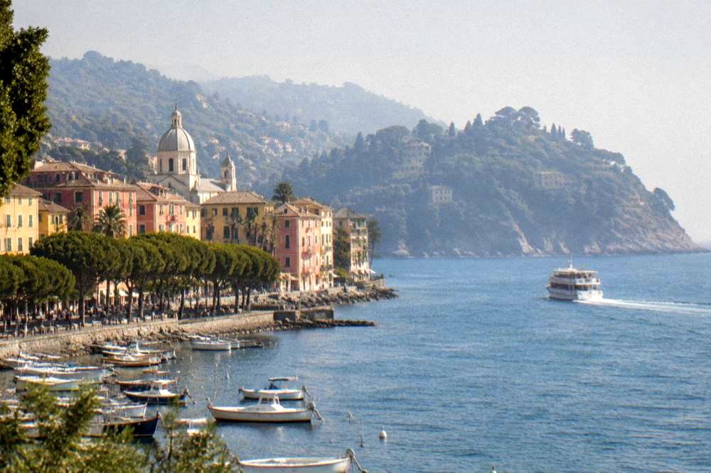 A passenger ferry crossing blue water towards the rocky headland of the Portofino promontory