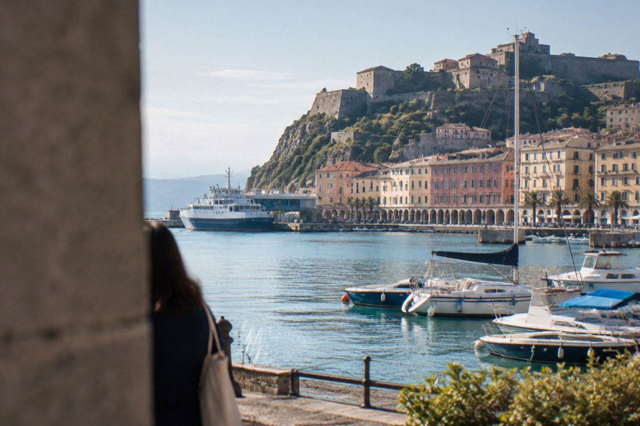 A stone fortress above a Ligurian harbour with boats moored below