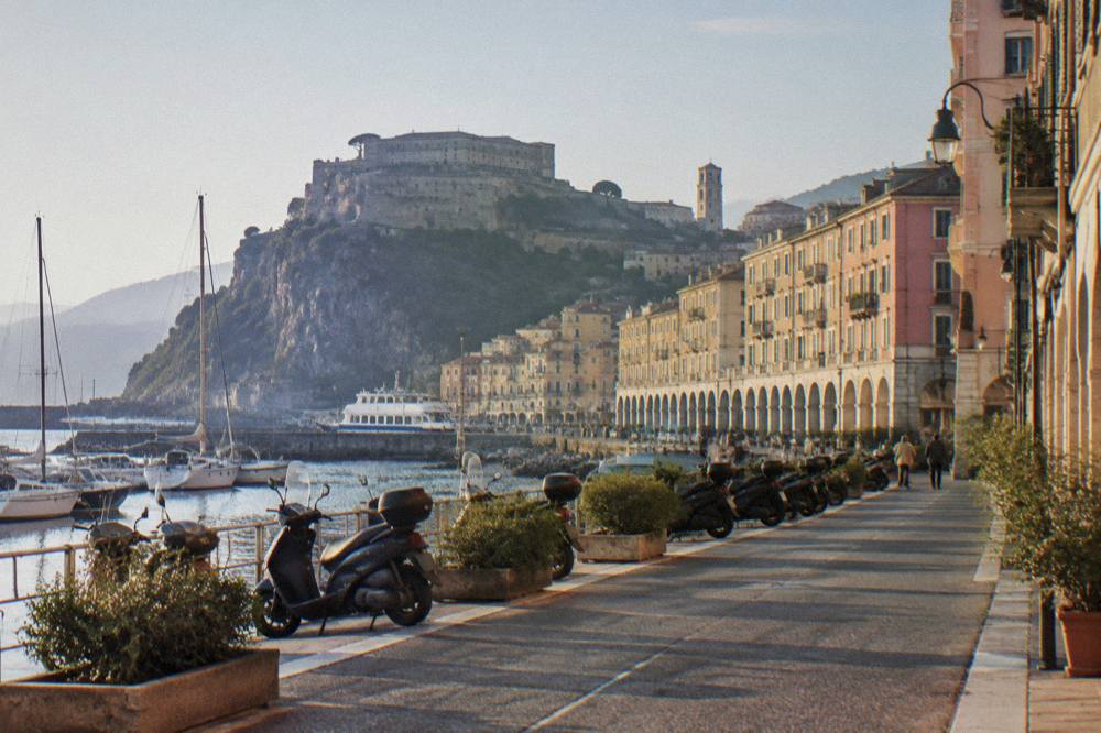 Pastel buildings along an Italian seaside street with parked scooters