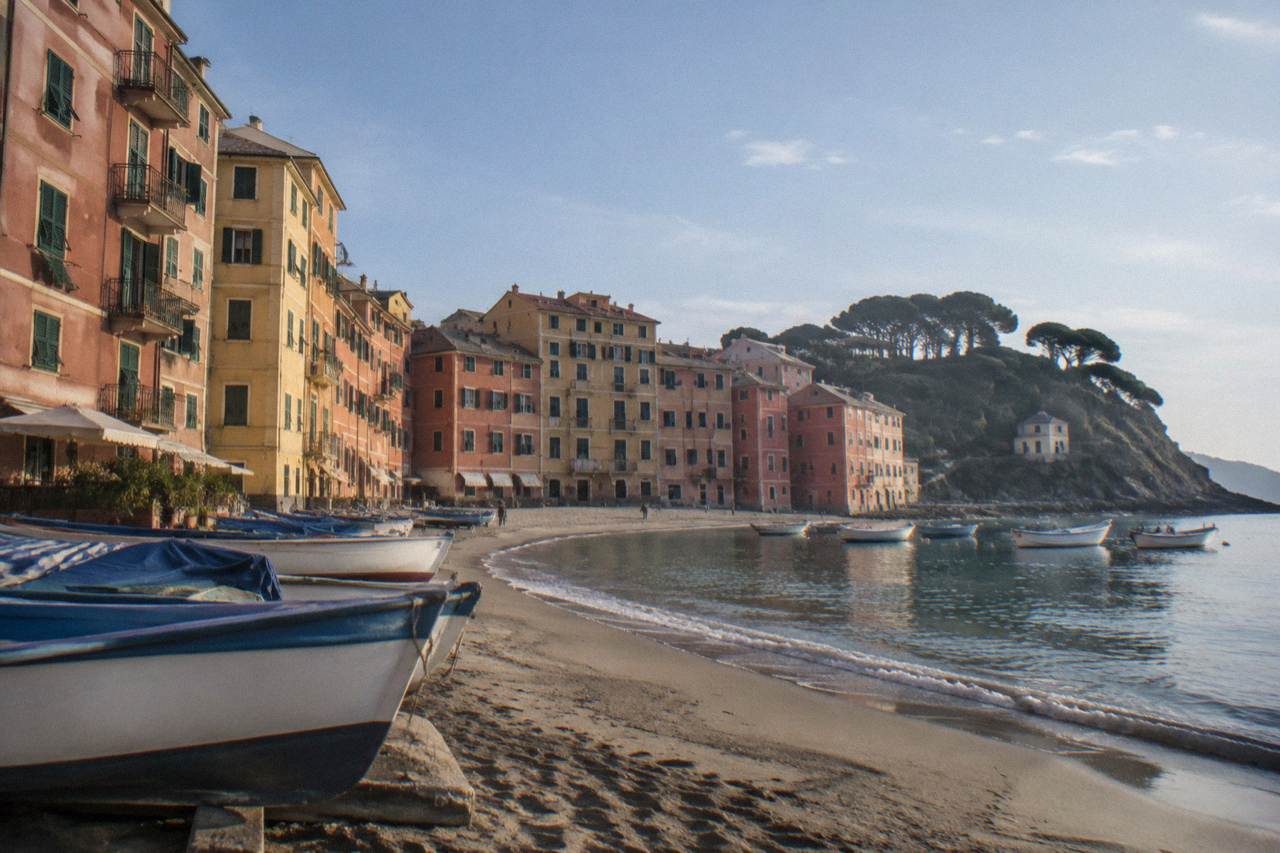 Colourful apartment buildings rising above a small sandy bay with fishing boats in Sestri Levante