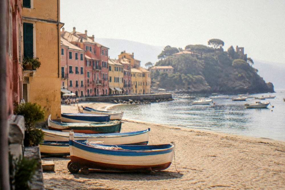 Small fishing boats resting on golden sand beside tall ochre and pink buildings at the Bay of Silence