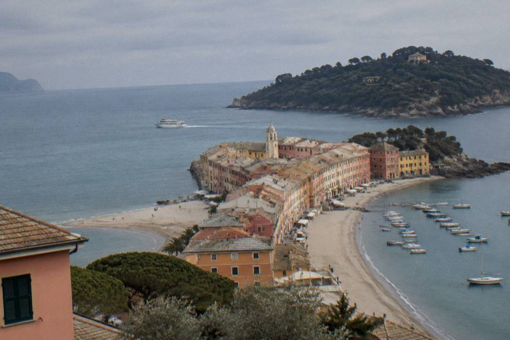 A small passenger ferry crossing blue water toward a wooded Ligurian headland