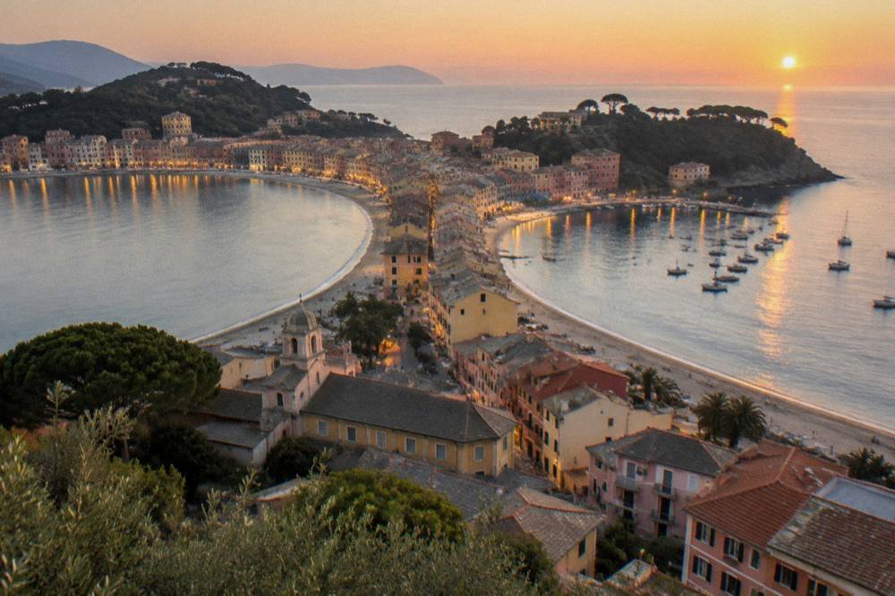 Wide view of a two-bay Ligurian town at dusk with lights reflected on calm water