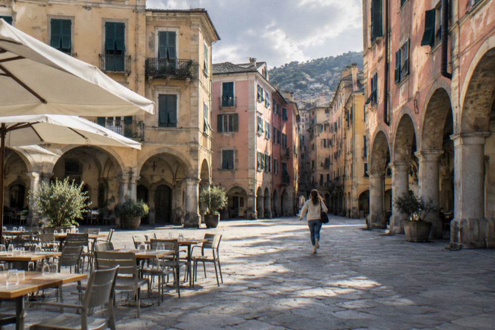 Outdoor tables with plain chairs and glasses under umbrellas on a small old-town square in the early evening, nobody seated