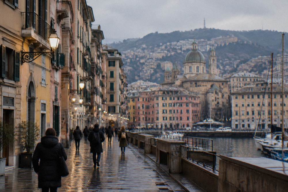 People in winter coats walking a wet lamplit street in central Genoa