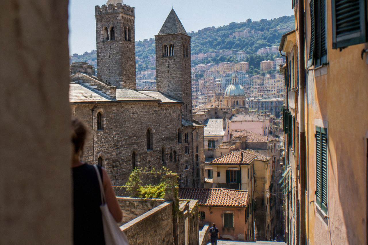 A stone medieval house and twin towers beside a narrow street in the old town of Genoa