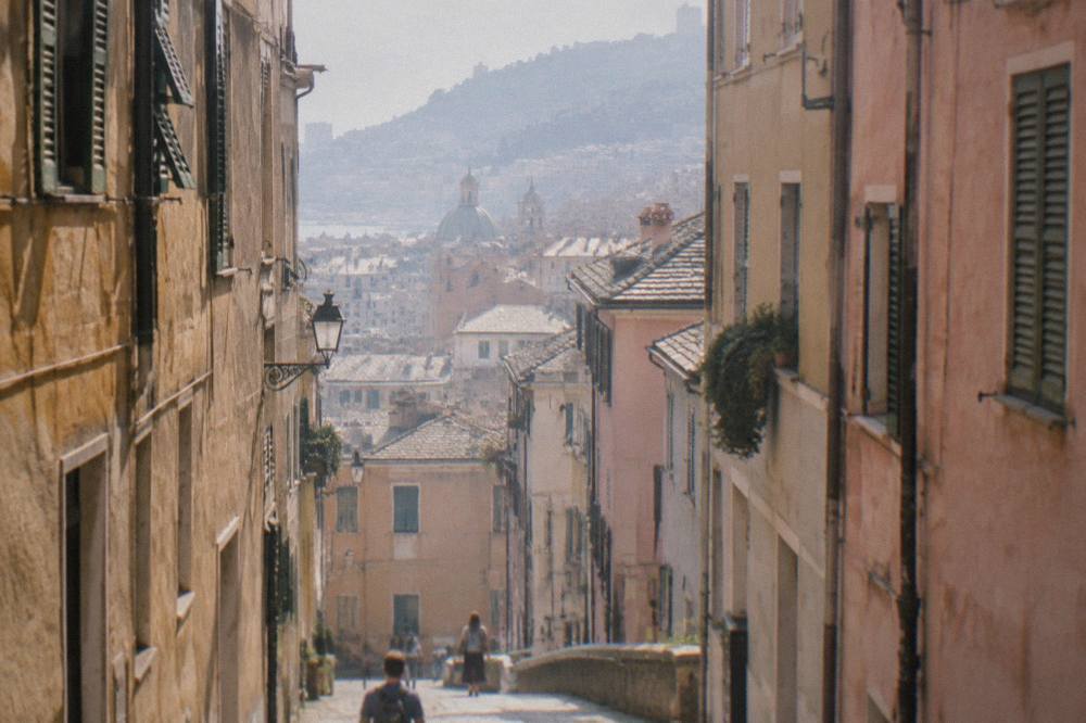 A narrow paved alley in the medieval old town of Genoa with tall old buildings on both sides