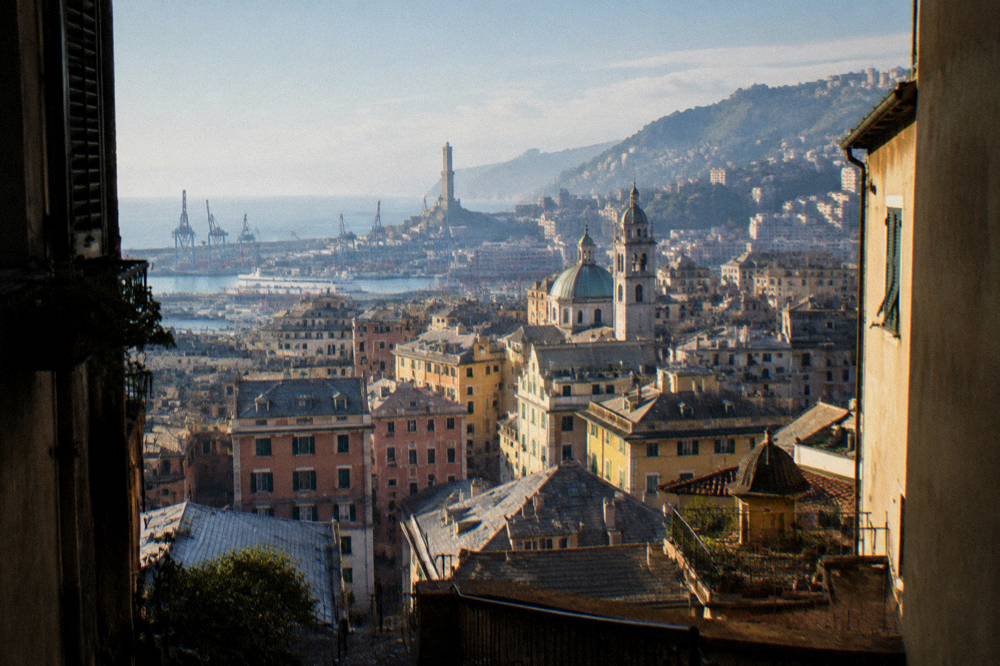 The tall white lighthouse of Genoa standing above the harbour cranes and rooftops