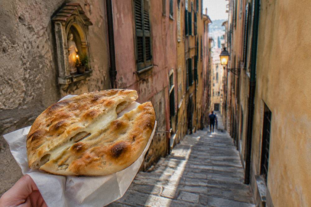 A round thin focaccia with a blistered golden crust, cut open to show melted cheese between two layers of dough