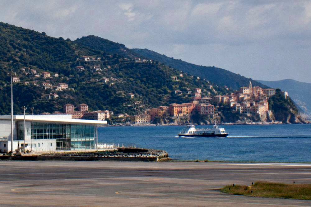 A ferry boat crossing blue water towards a village of coloured houses on a headland