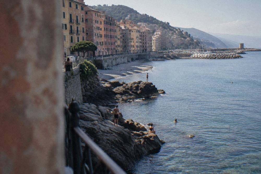 People swimming from flat rocks into clear water below a cliff path
