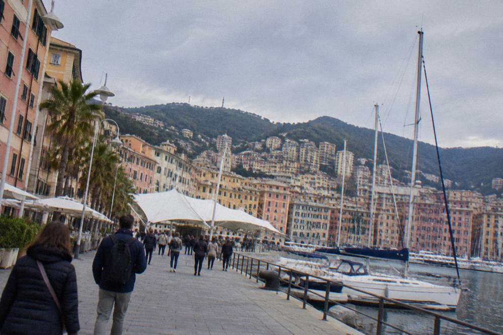 Crowds walking along a waterfront promenade lined with moored sailing yachts