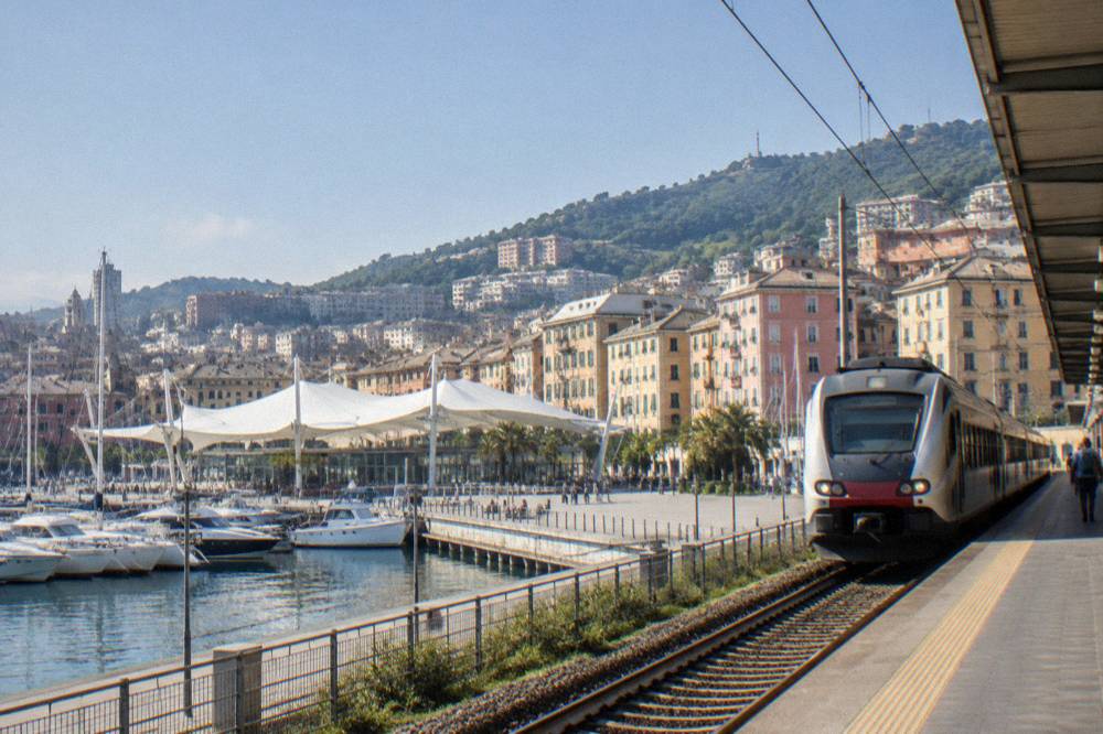 A passenger train pulling into an Italian railway station beside a seafront