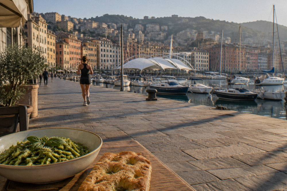 A bowl of green basil pasta beside flat focaccia bread on a wooden table