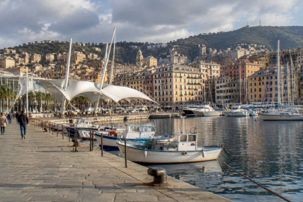 A small pastel-coloured fishing village seen from the water with wooded hills behind