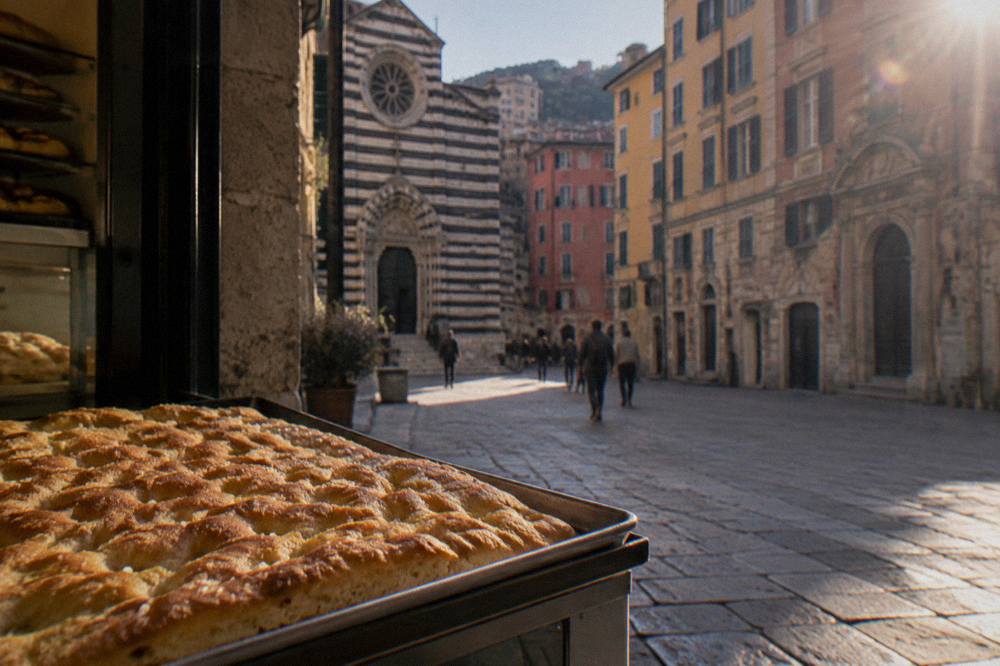 A flat tray of golden Genoese focaccia with dimples and sea salt on a bakery counter