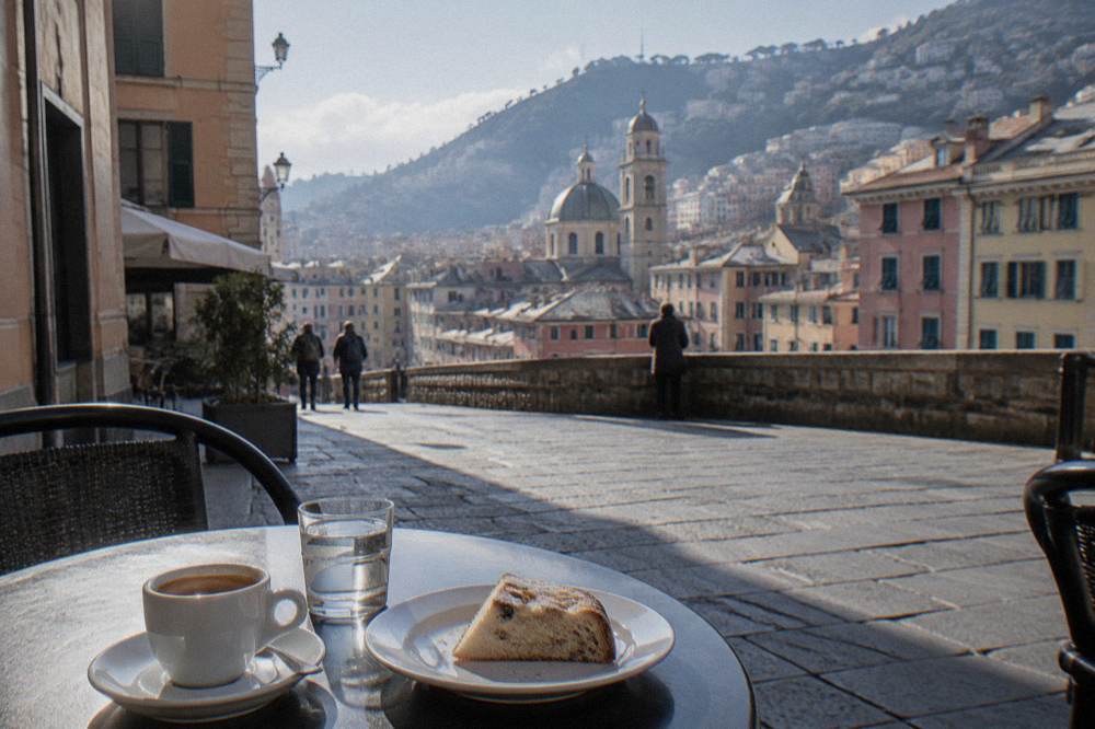 A table in a Genoa café with an espresso cup, a glass of water and a slice of sweet bread