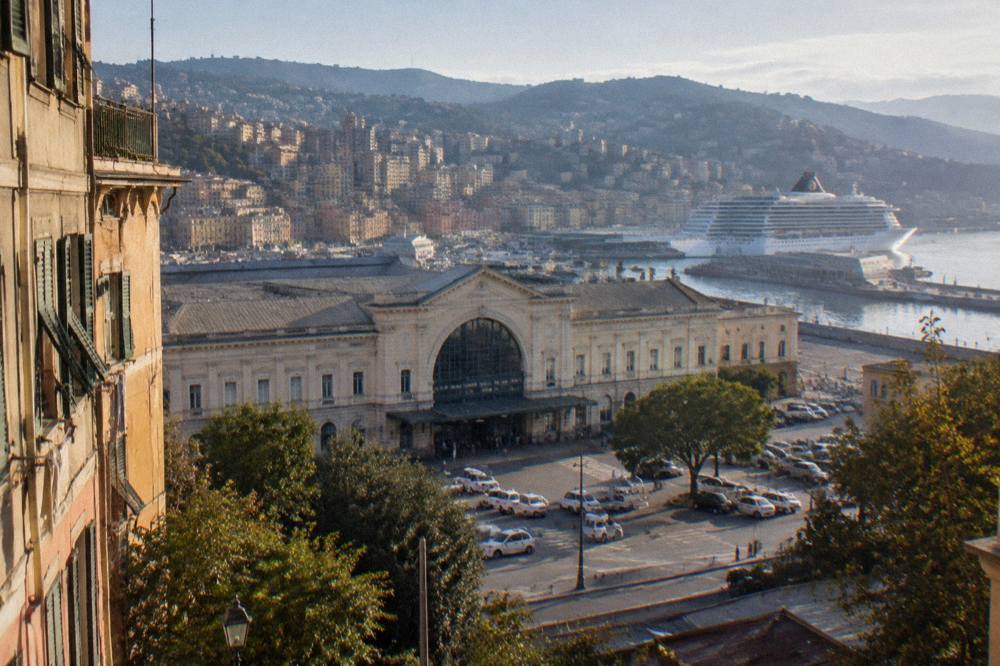 A large cruise ship docked at a terminal pier beside a hillside city