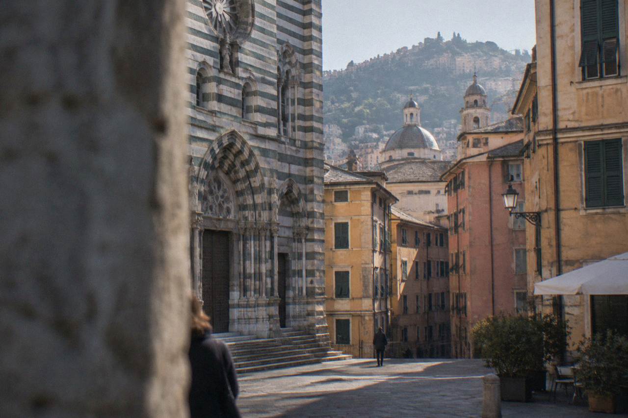 Striped stone facade of a historic church in Genoa seen from a narrow square