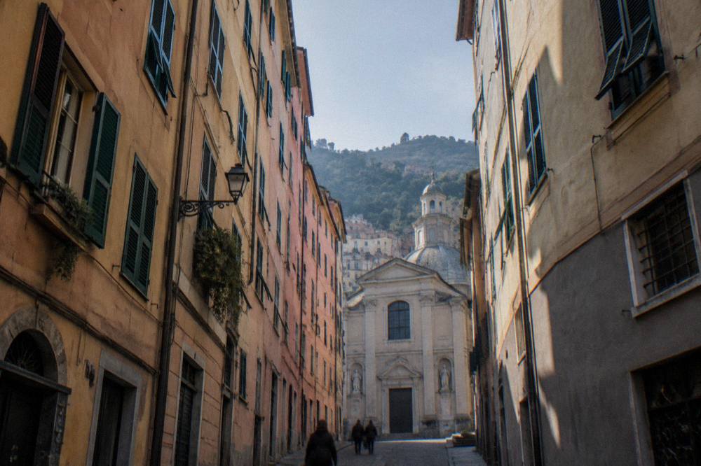 Narrow Genoa street with a church facade rising at the end of the lane