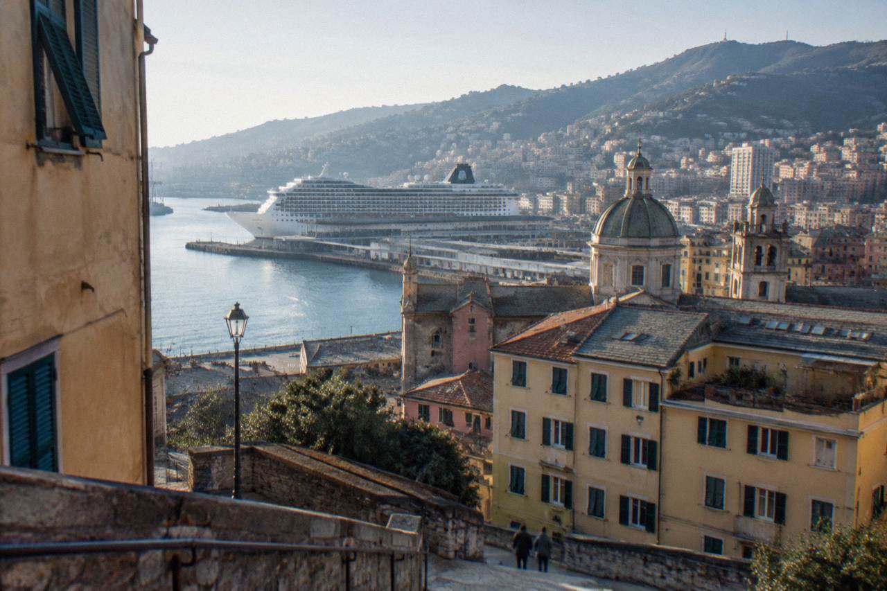 Cruise ship docked at a terminal in the port of Genoa with hills rising behind the harbour