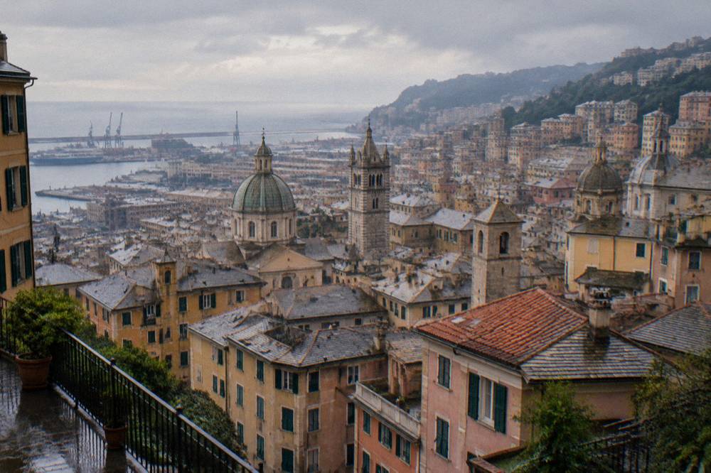 View over the rooftops and towers of central Genoa toward the sea from an elevated terrace