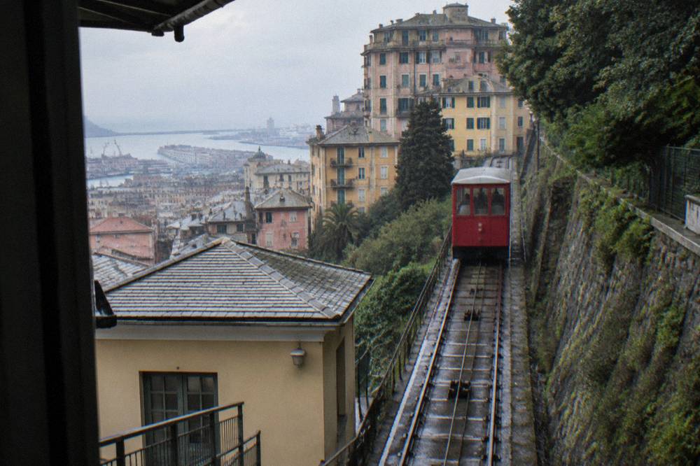 A red funicular car climbing the Zecca-Righi track through Genoa's hillside buildings