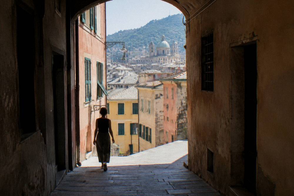Person walking empty-handed down a narrow covered alley in Genoa's old town