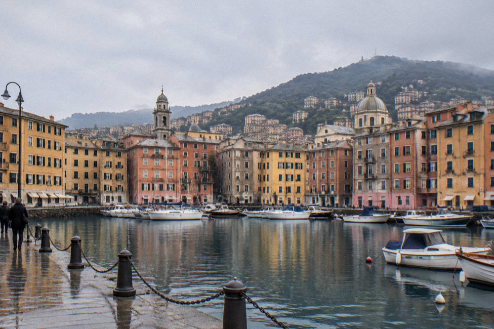 Boats moored in a small Ligurian harbour beneath pastel-coloured waterfront buildings