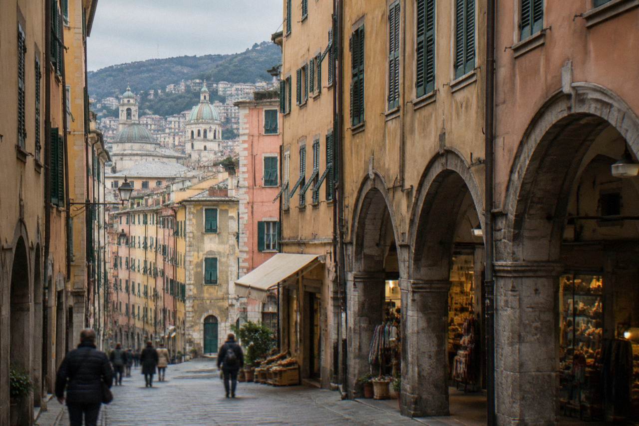Narrow old town street in Genoa with tall coloured buildings and shops under stone arches