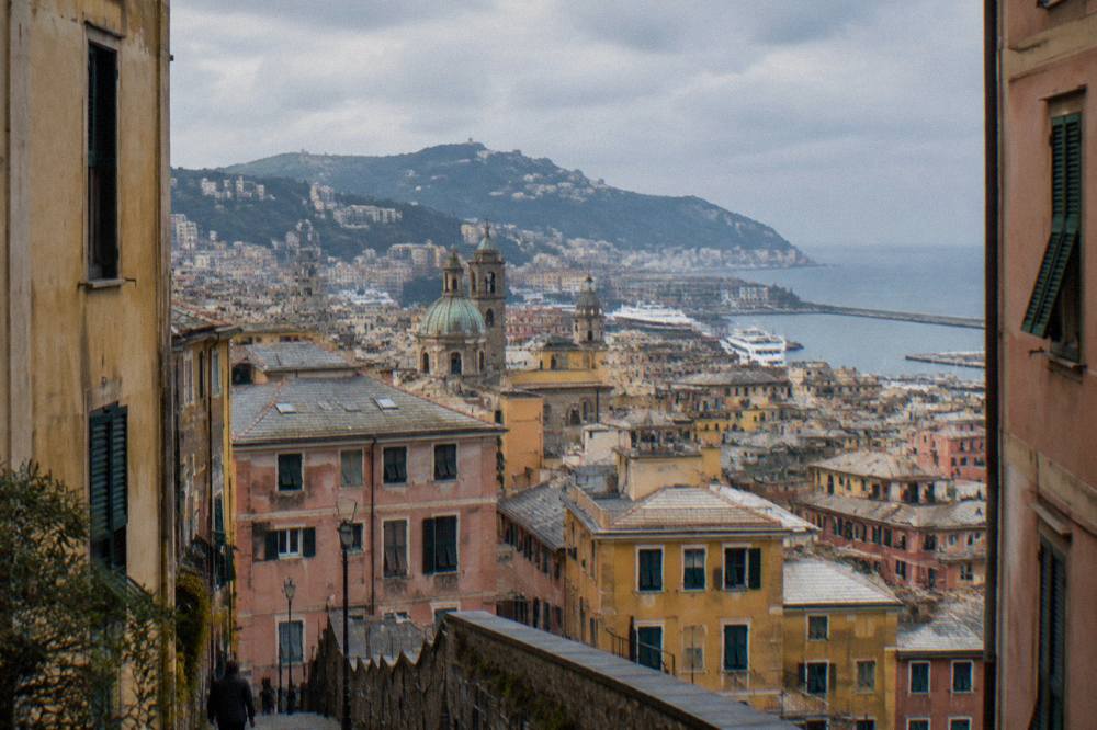 Terracotta rooftops of Genoa descending toward the sea with hills behind