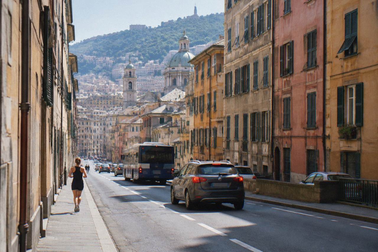 Cars and buses moving along a narrow street between tall coloured buildings in Genoa