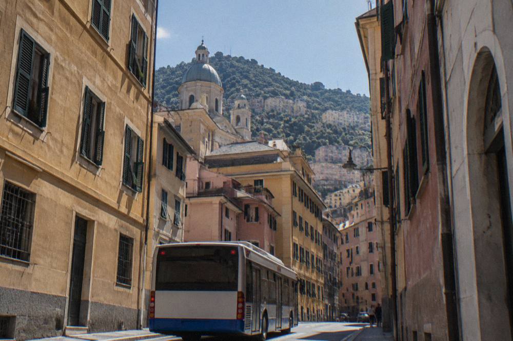 A city bus driving along a narrow street in central Genoa