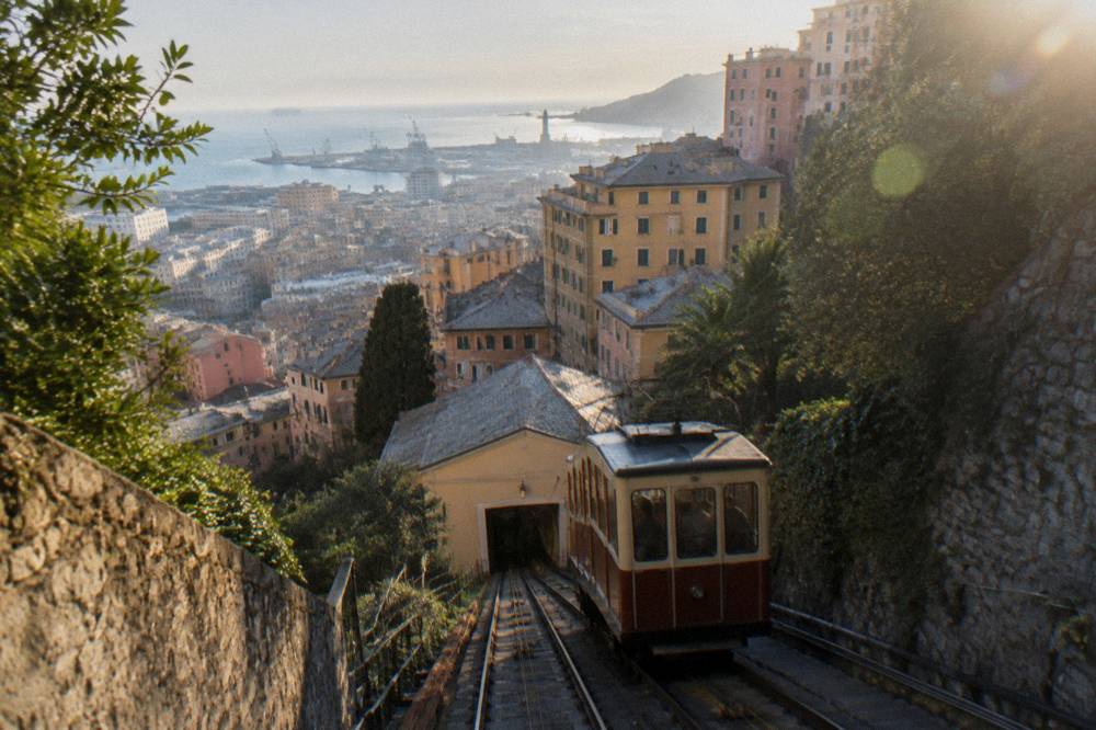 A funicular carriage climbing a steep hillside track above Genoa rooftops
