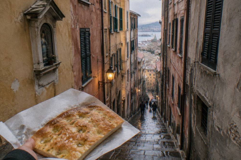 A flat rectangular piece of Genoese focaccia with olive oil and coarse salt on a paper sheet