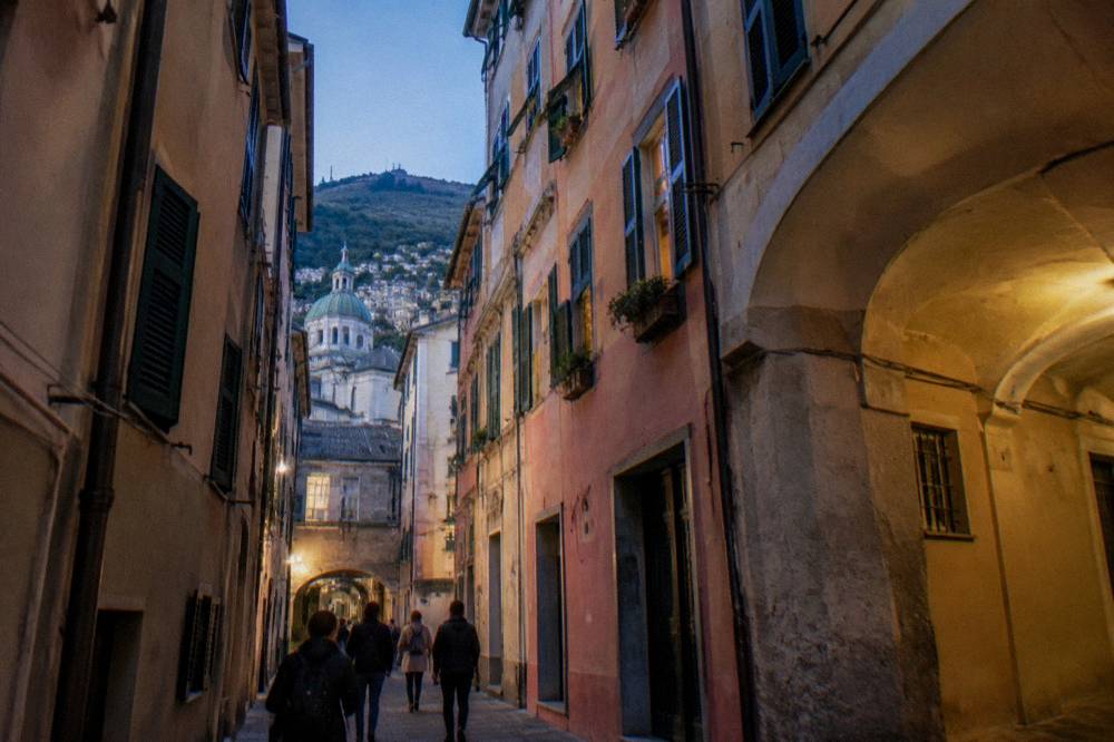 People walking a narrow covered lane in the old town of Genoa on a mild day