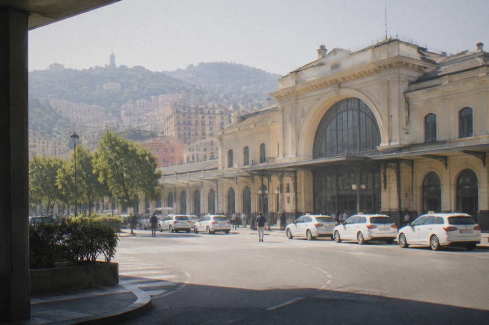 The exterior facade of a large Italian railway station with taxis waiting outside