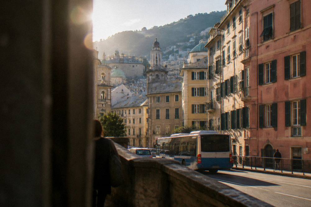 A Genoa street near a station with tall painted buildings and a bus passing