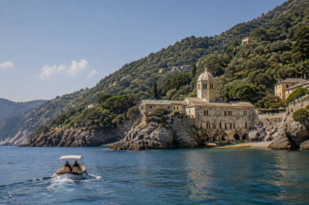A small boat approaching a rocky cove with an abbey on the Ligurian coast