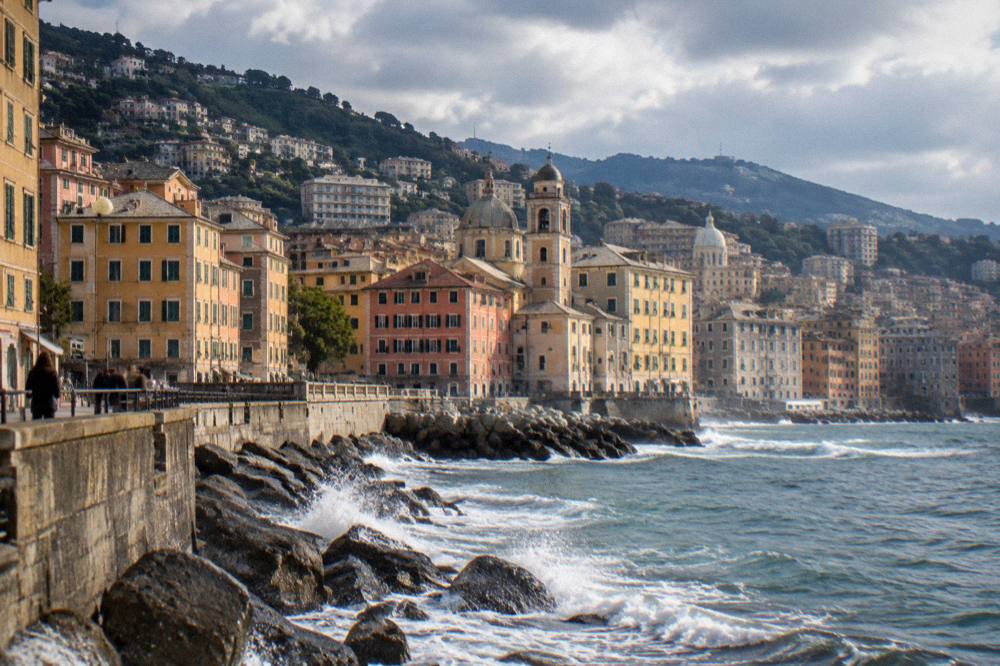 Waves breaking against rocks on a seaside promenade in Genoa under a cloudy sky