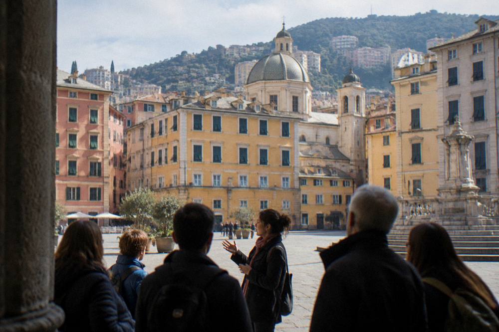 A storyteller guide leading a small group through a sunlit Genoa square
