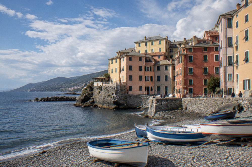 A rocky coast with a cliff-top promenade under fast-moving cloud and patches of bright sun, the sea a dark blue