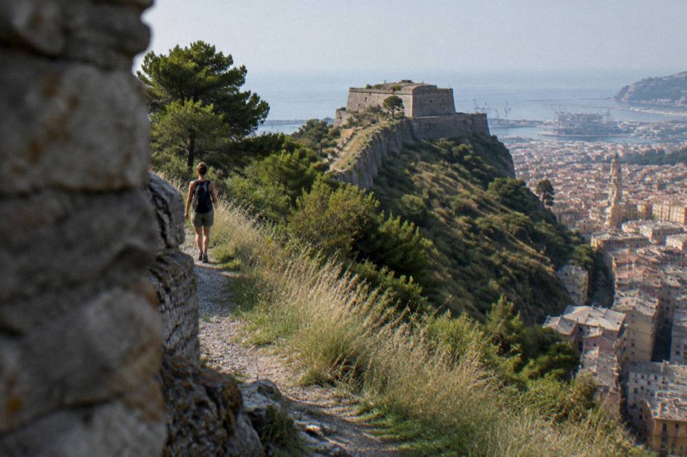 A walker with a small backpack on a ridge trail above the sea at midday