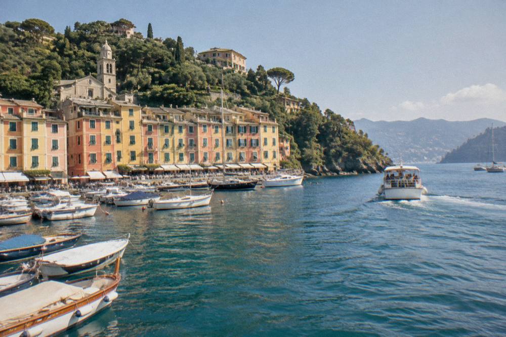 A passenger boat leaving a harbour toward wooded headlands on the Ligurian coast