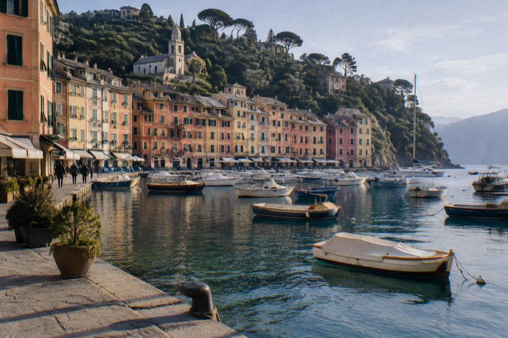 A small harbour ringed by tall coloured houses with moored boats in clear water