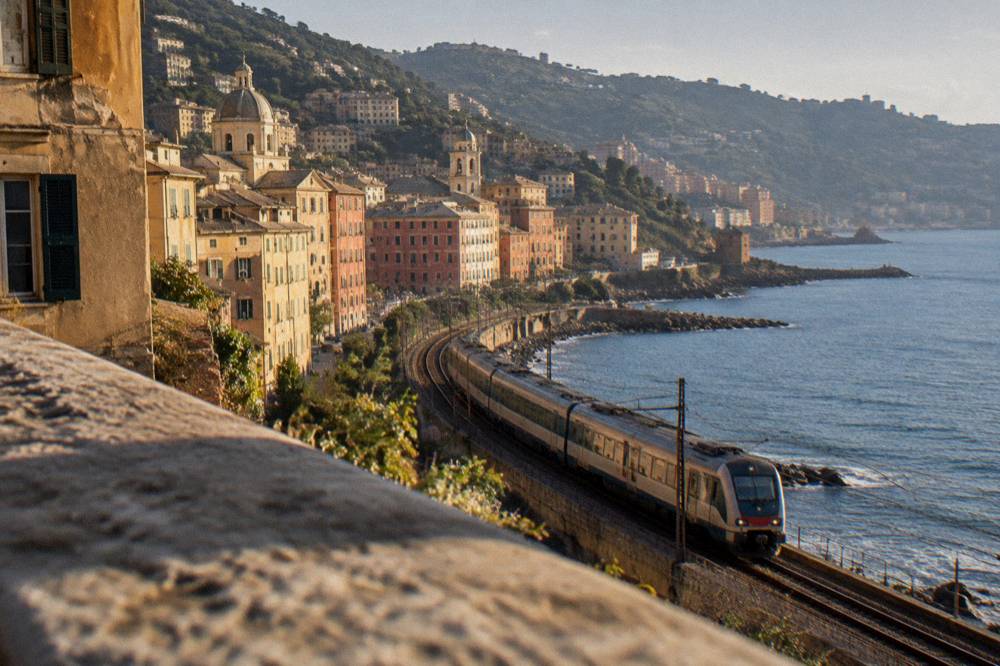 Regional train departing along the Ligurian coast with the sea on one side of the tracks