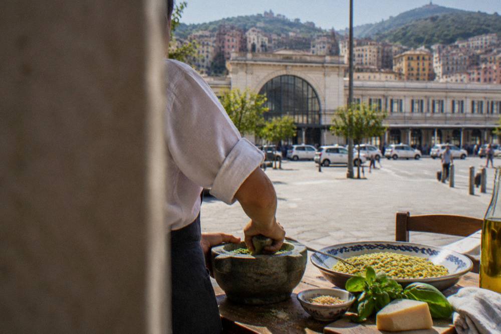 Green basil pesto being mixed in a stone mortar with pasta on a wooden table